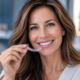 Adult woman smiling and holding a clear Invisalign aligner