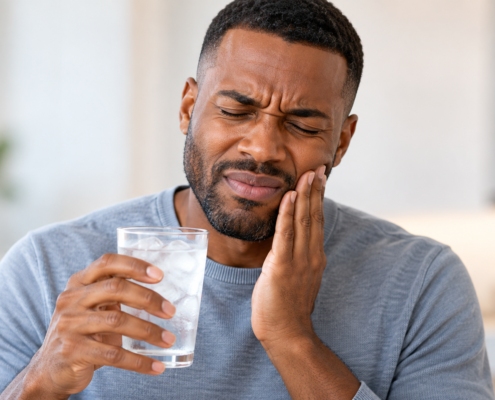 Man experiencing sudden tooth sensitivity while holding a glass of ice water.